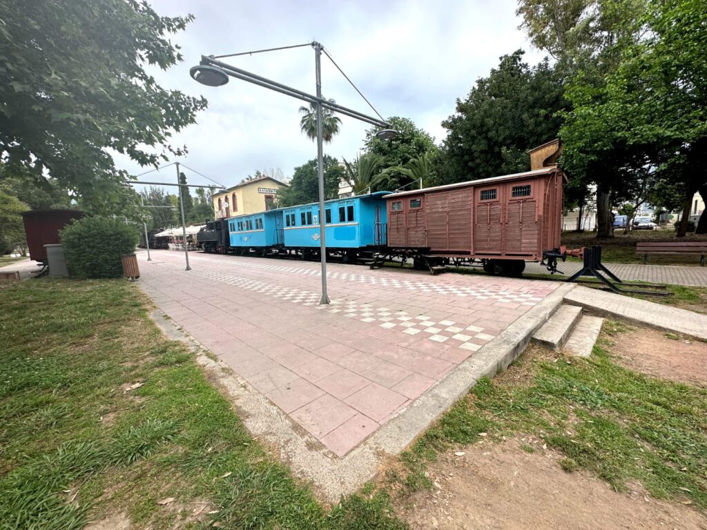 Scenic view of Kalamata Railway Park featuring well-maintained train tracks, vintage locomotives, and lush green surroundings, offering a peaceful and historical atmosphere.