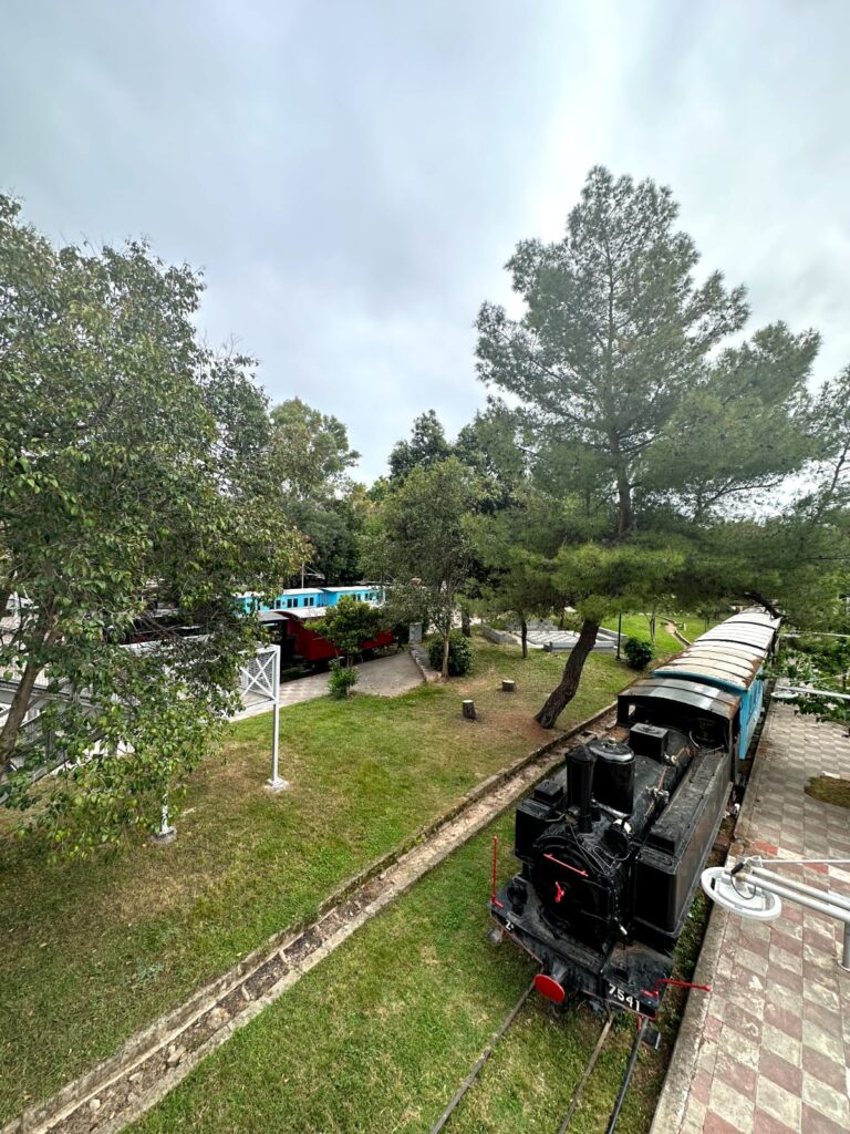 Historic old trains displayed at the Municipal Railway Park in Kalamata, Greece, showcasing vintage locomotives and carriages amidst a backdrop of lush greenery and railway tracks.