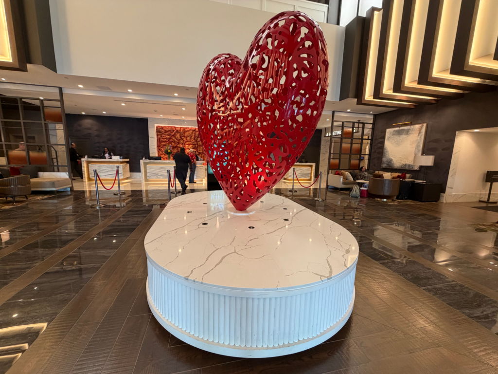 A prominent metal heart installation in the center of the hotel lobby, reflecting the ambient lighting of the casino and symbolizing top-tier guest service.